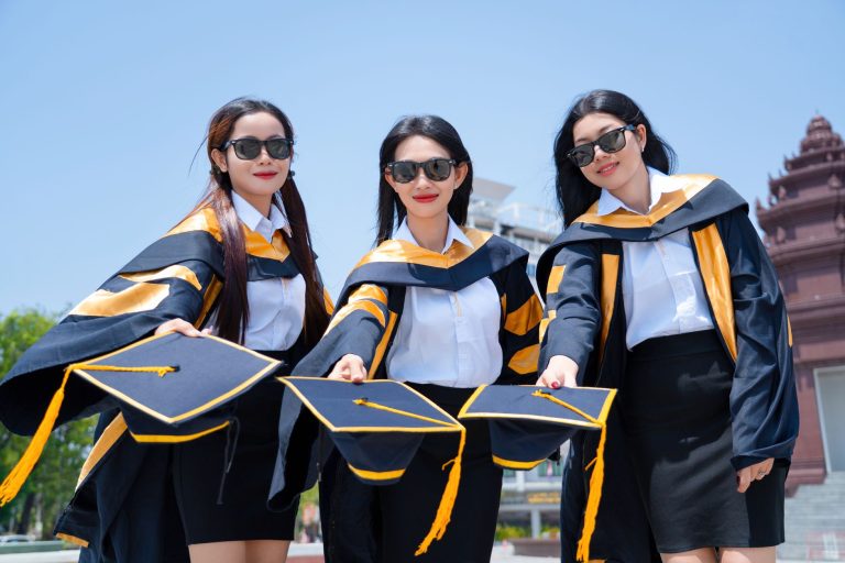 Three graduates in gowns holding their graduation caps outdoors