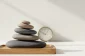 Stack of smooth stones on a wooden tray with a blurred analog clock, set against a soft neutral background, symbolizing balance and routine.