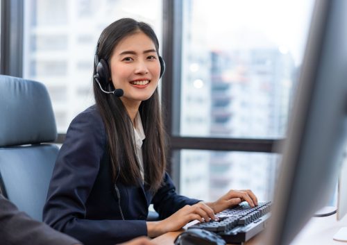 Happy smiling operator Asian woman customer service agent with headsets working on computer in a call center, talking with customer for assisting to resolve the problem with her service mind